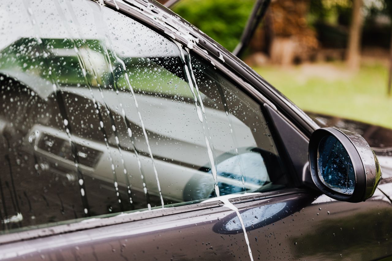 Detail of a car window with soap and water at an outdoor car wash.